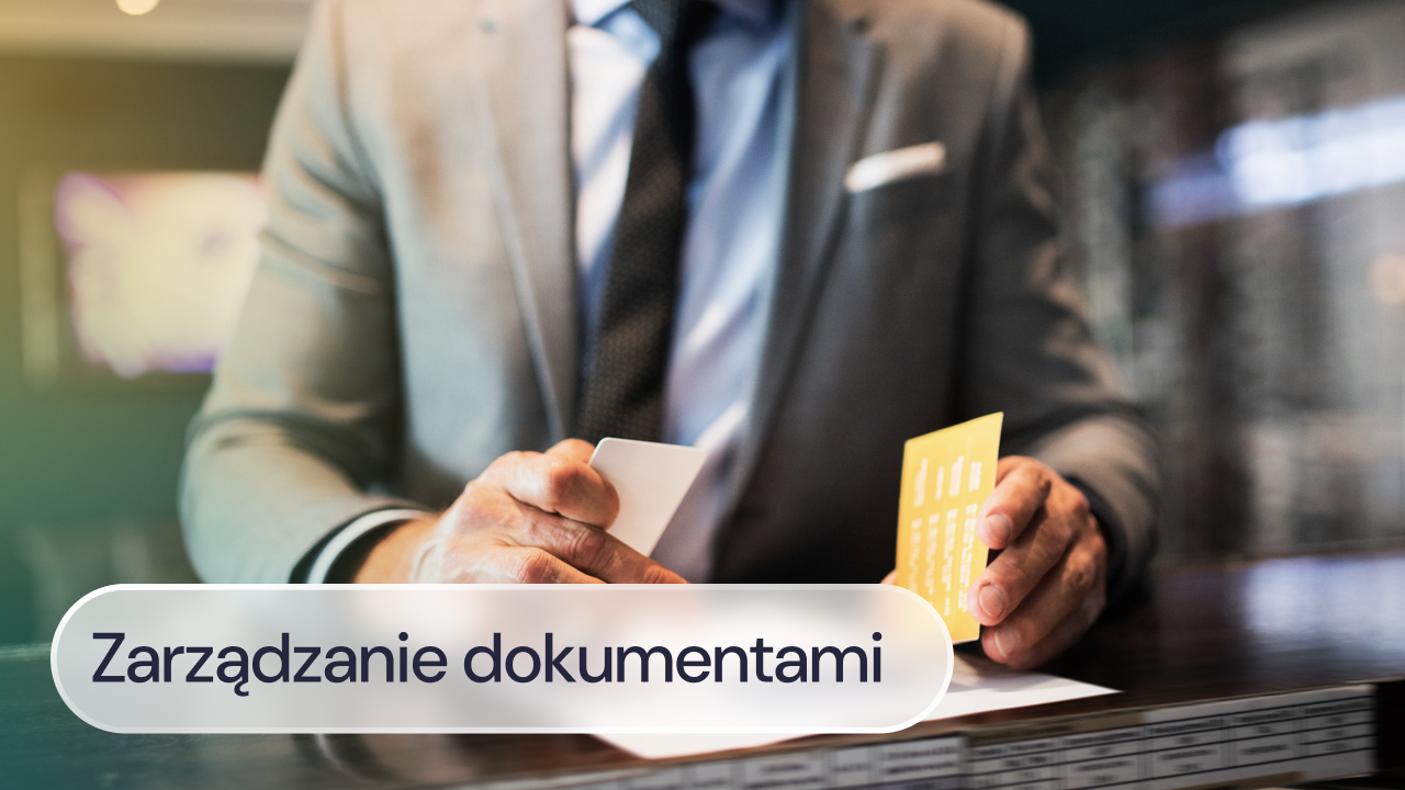 Pracownik w garniturze trzyma dokumenty przy biurku.