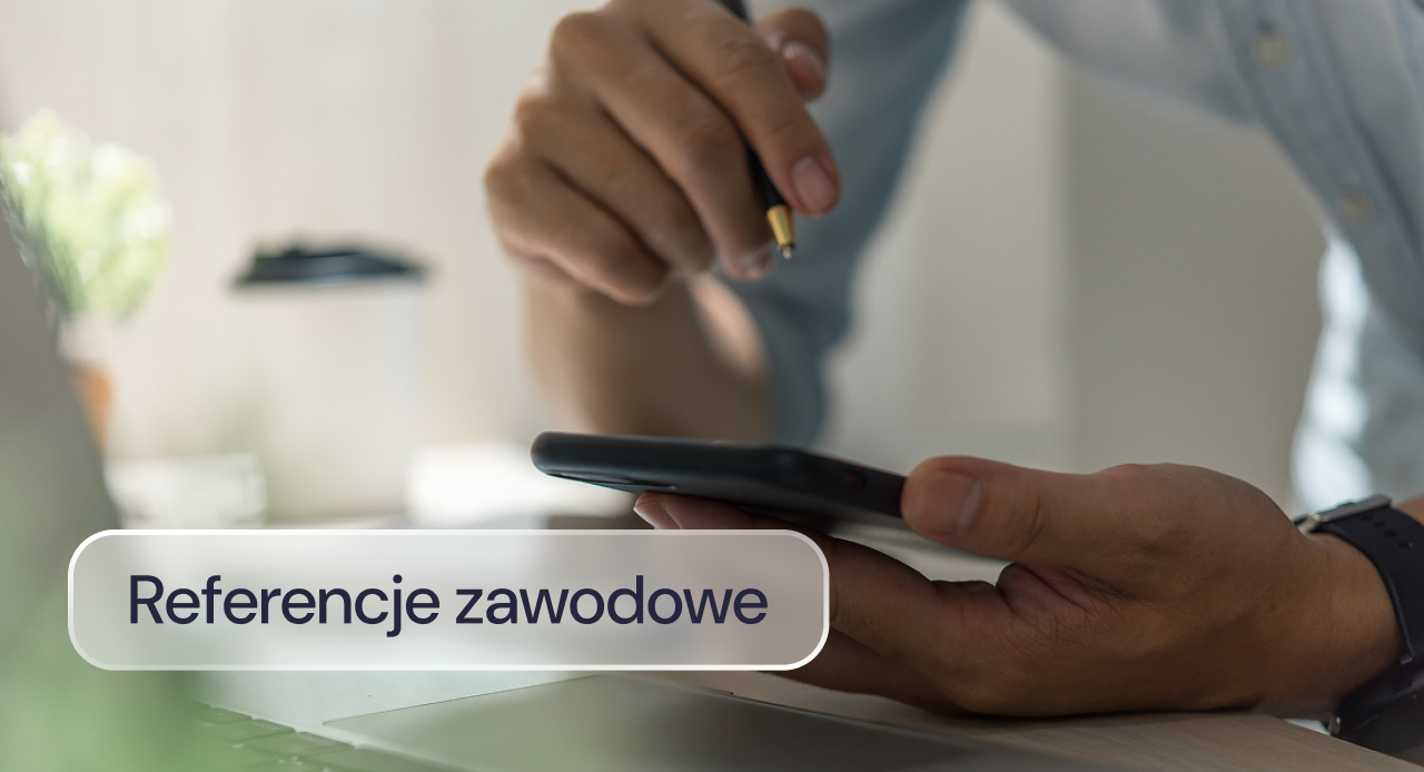 Pracownik trzyma telefon i długopis nad laptopem w trakcie pracy.