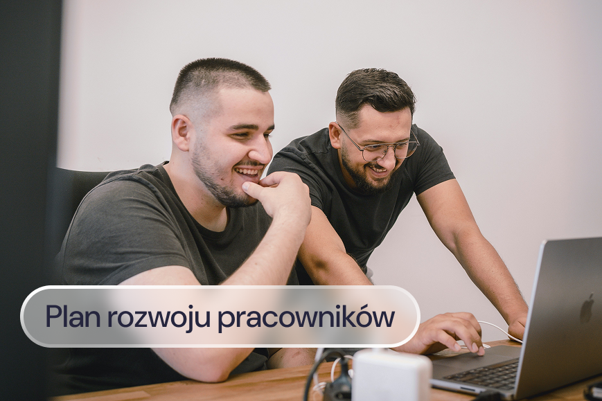 Dwóch mężczyzn uśmiecha się podczas wspólnej pracy przy laptopie.