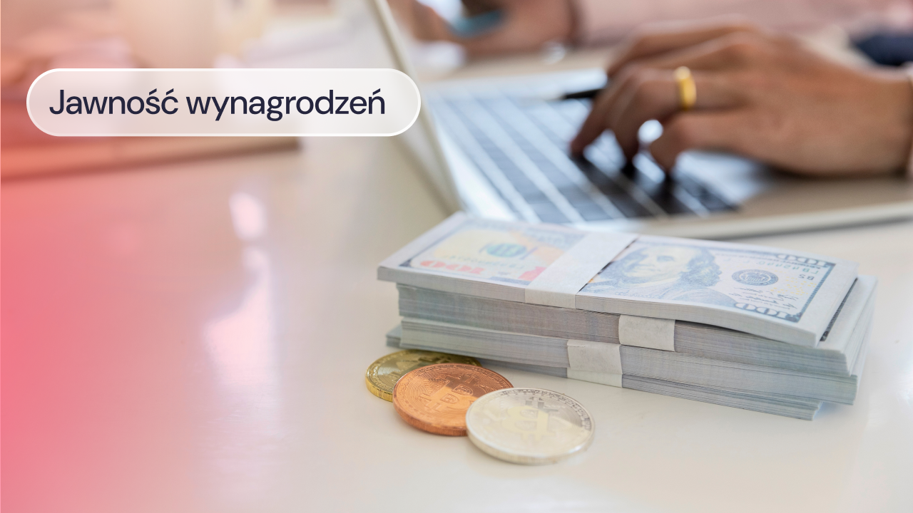 Plik banknotów i monety leżą na biurku obok laptopa.