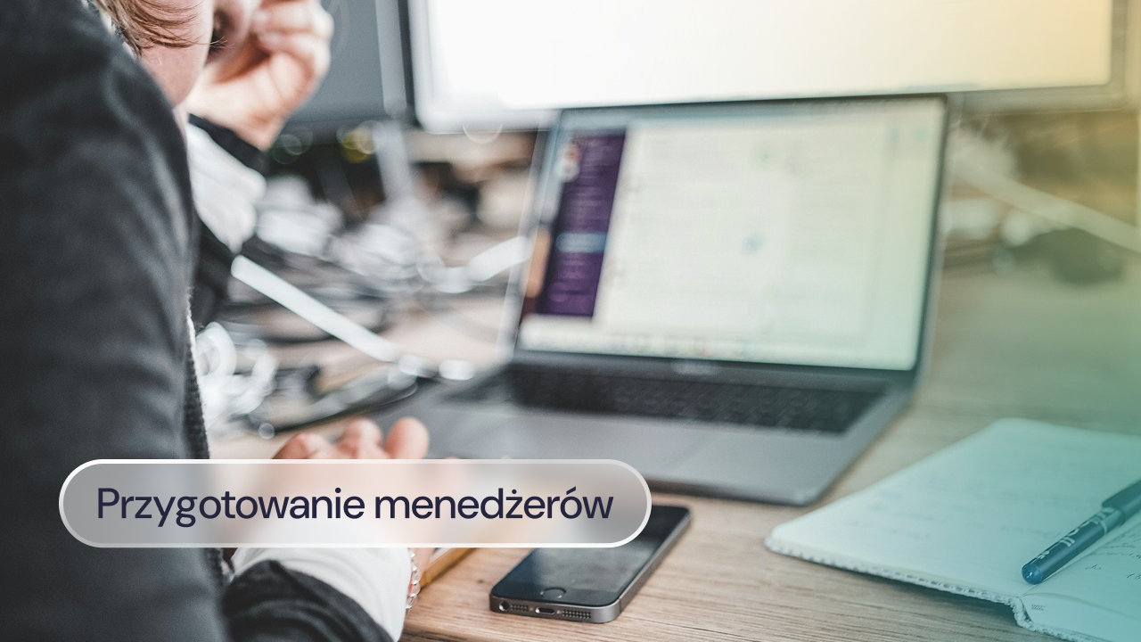 Pracownik przy laptopie z telefonem i notatnikiem na biurku.