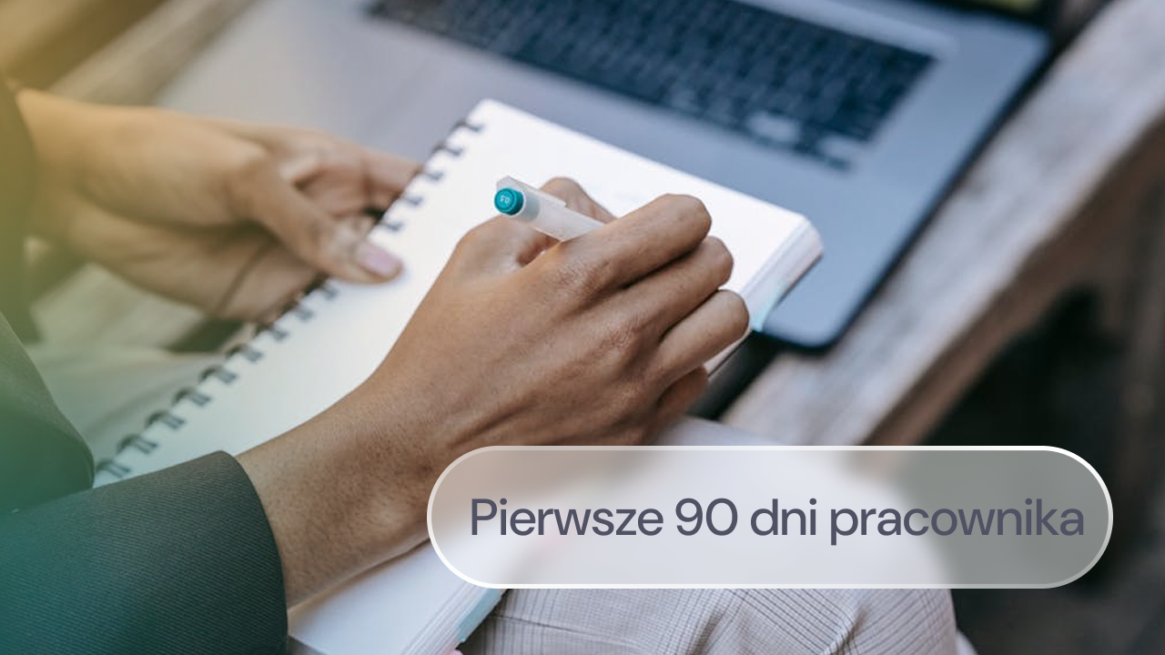 Pracownik robi notatki w zeszycie i pracuje przy laptopie.